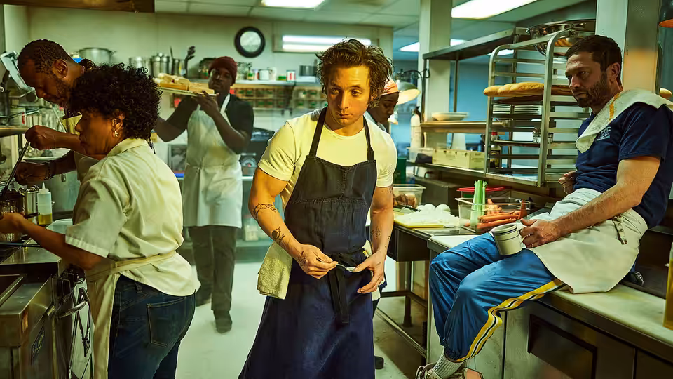 Carmy (Jeremy Allen White) adjusts his apron in a busy kitchen as staff work around him