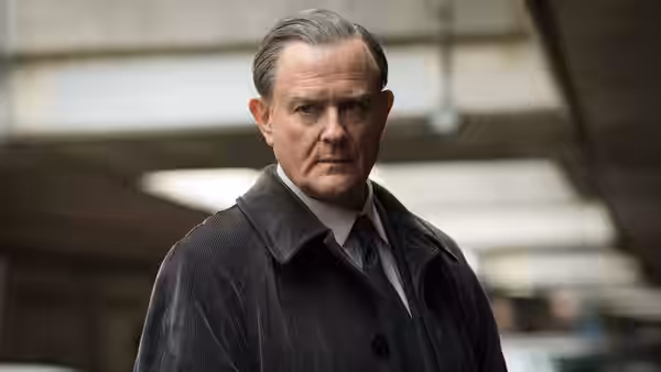 DCI Brian Boyce (Hugh Bonneville) in a dark coat outdoors under concrete
