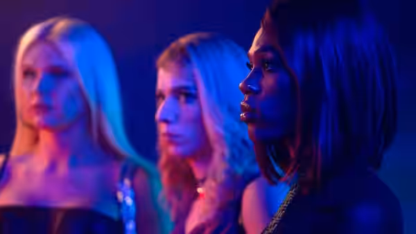 Three women stand close together under blue and purple club lighting
