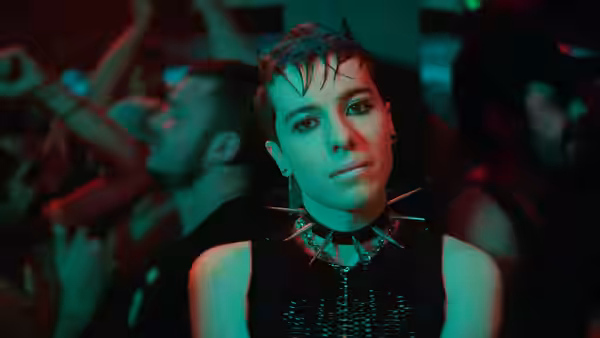 Young person with spiked collar stands in a neon-lit nightclub crowd