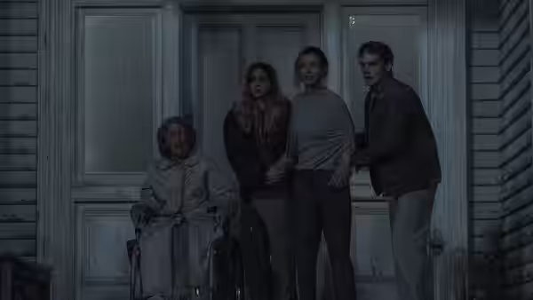 Four people stand on the porch of a house one seated in a wheelchair