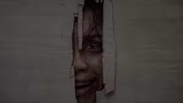 A dirty-faced woman peers through a torn hole in a wall