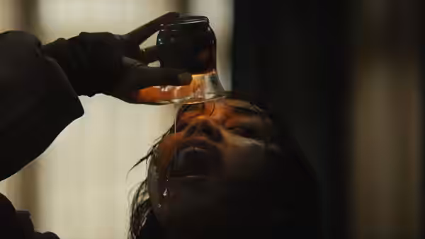 A gloved hand pours liquid from a jar into a woman's open mouth