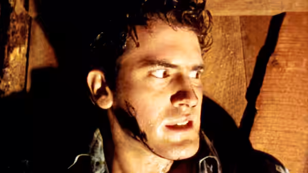 A young man looks anxiously to the side in a dim wooden room