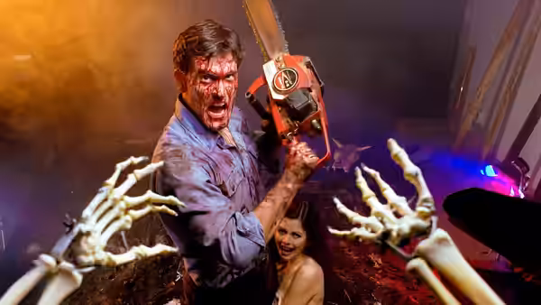 Ash (Bruce Campbell) raises a chainsaw as skeletal hands reach toward him and a woman crouches behind