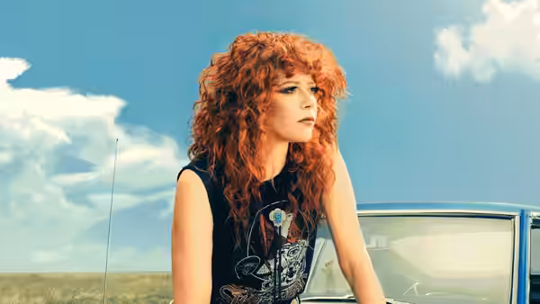 Charlie Cale (Natasha Lyonne) leaning against a car under a blue sky