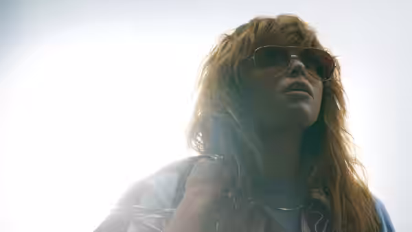 Charlie Cale (Natasha Lyonne) wearing sunglasses and looking upward against bright sky
