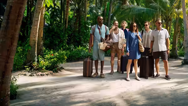 Six travelers walking with luggage along a shaded jungle path