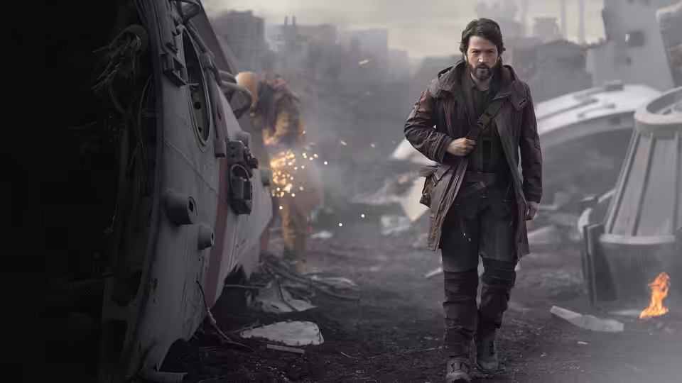 Cassian Andor (Diego Luna) walking past a damaged spacecraft in ruins