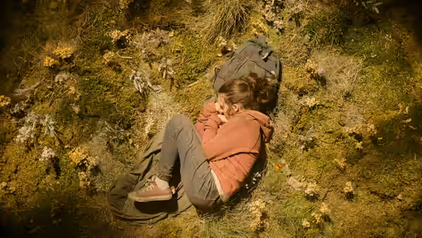 Ellie (Bella Ramsey) lying on mossy ground with backpacks