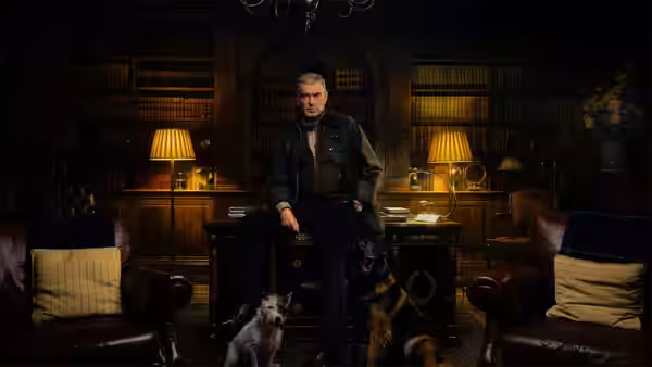 Conrad Harrigan (Pierce Brosnan) sitting in a library with dogs at his feet
