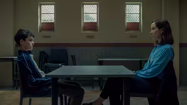 A boy and a girl sitting opposite each other at a table in a sparse room