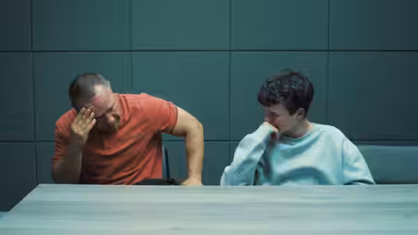 A man in a red shirt and a boy in a sweatshirt at a table