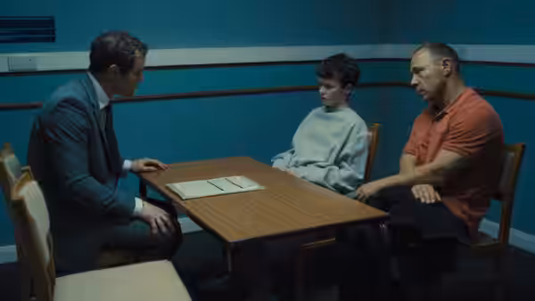 Three men seated around a wooden table in a blue interview room