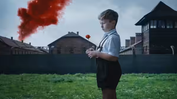 Young boy stands holding flower with red smoke in sky
