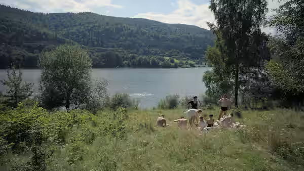People picnic and swim near lake with hills in background
