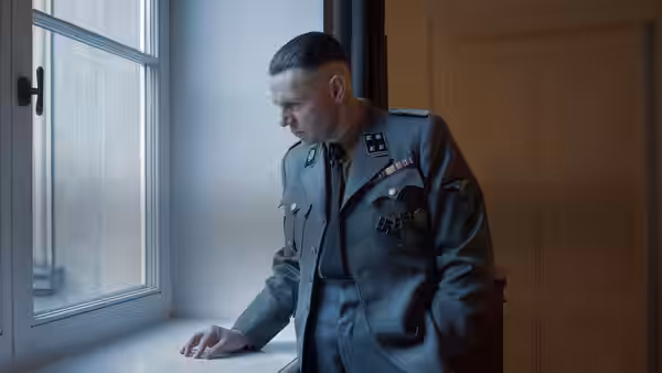 Rudolf Höss (Christian Friedel) leans against windowsill in uniform