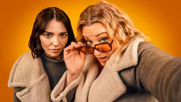 Two women in fleece jackets take a close-up selfie, one holding sunglasses