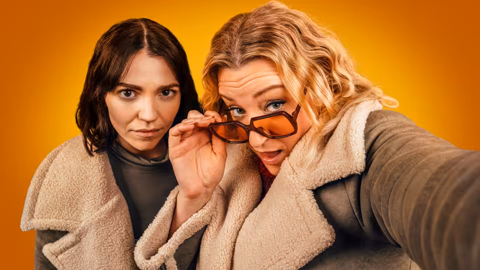 Two women in fleece jackets take a close-up selfie, one holding sunglasses