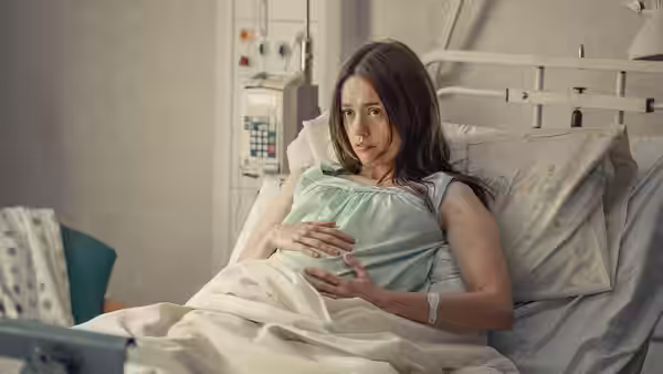 A pregnant woman resting in a hospital bed with hands on her belly