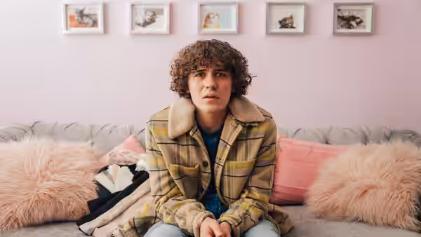Young man with curly hair sits on a grey sofa looking ahead