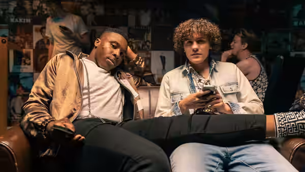 Two men relax on a couch while one checks his phone