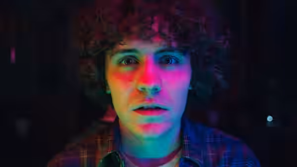 Close-up of young man with curly hair under pink and blue lights