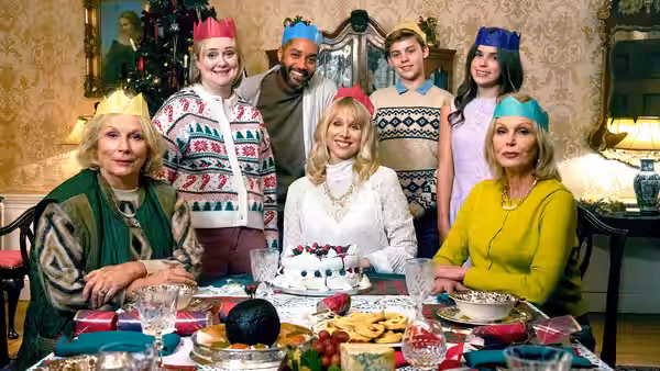 Adults and teenagers in party hats gathered around a Christmas dinner table with cake