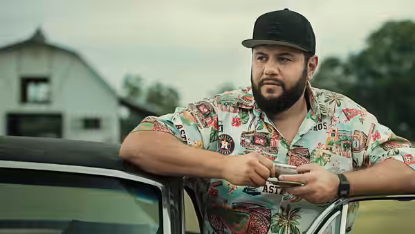 Mohammed Amer as Mo Najjar leaning on a car while looking at his phone