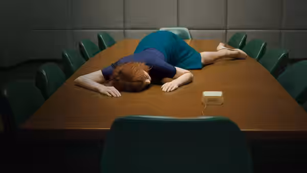 Woman lying face down across a long wooden conference table