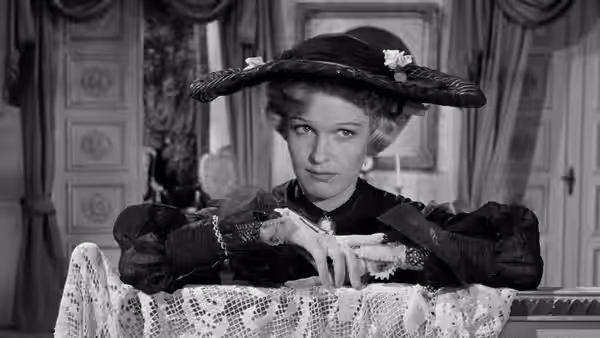 A woman in a broad hat adjusts her gloves at a table