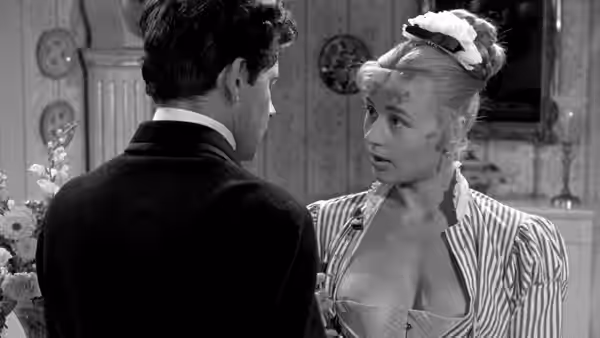 A dark-haired young man faces a blonde woman in a striped jacket