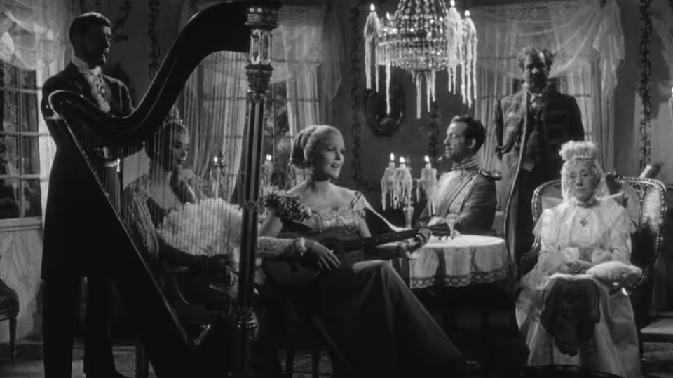 A harpist plays as guests gather around a table in an elegant drawing room