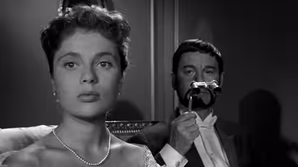 A woman sits in the foreground as a man peers through an opera glass behind her