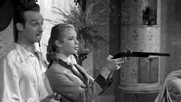 A woman in a riding jacket aims a pistol as a man watches