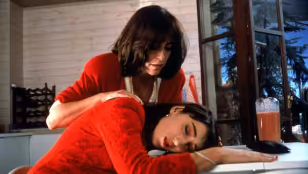 Woman in red cardigan leans over woman lying on kitchen counter