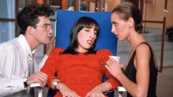 Man and two women surround woman in red seated in blue chair