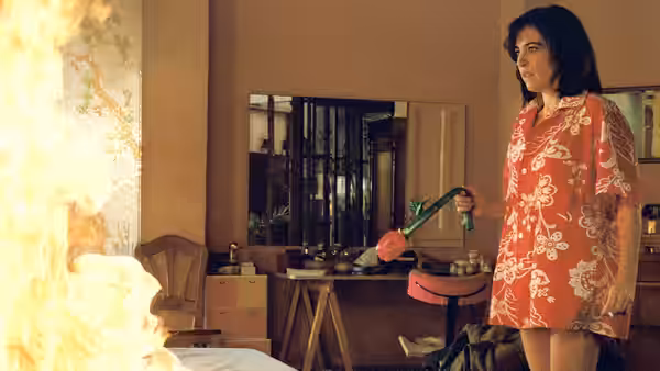 Woman in floral robe holds phone receiver near burning room fire