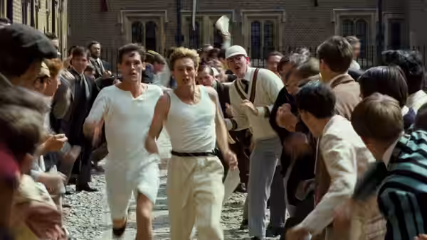 Two runners in white singlets dashing through a crowded college courtyard