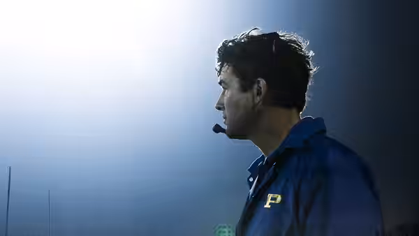 Eric Taylor speaks into a headset under bright stadium lights