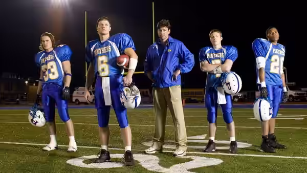 Eric Taylor stands with four Panthers players on the night football field
