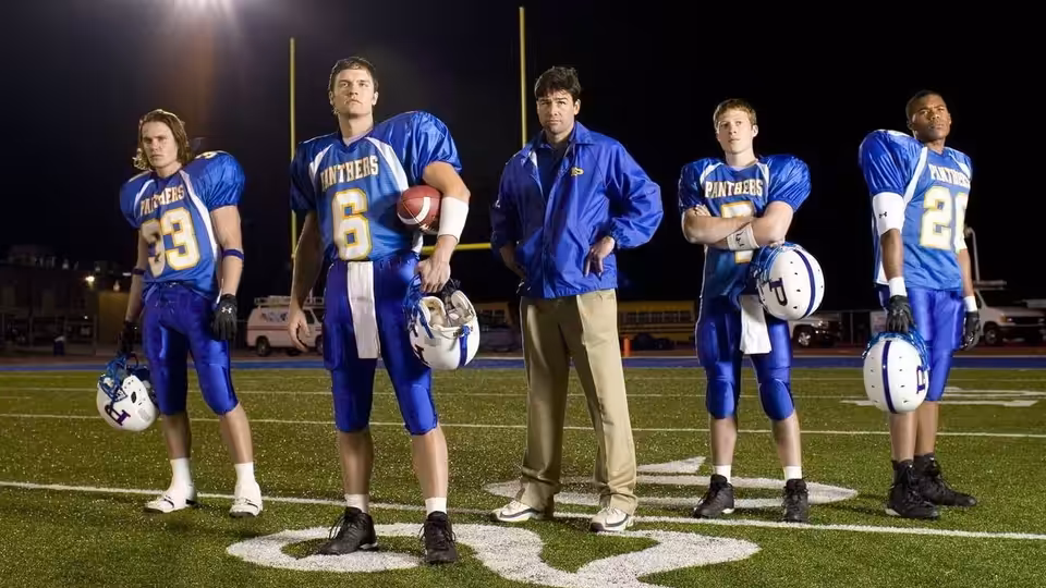 Eric Taylor stands with four Panthers players on the night football field