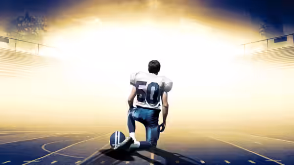 Football player number 50 kneels with a ball on the field at sunset