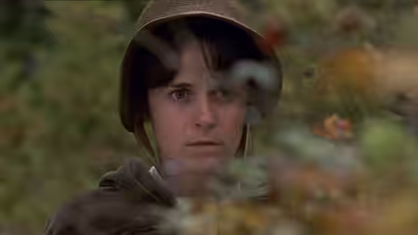Anne (Amanda Root) peers through foliage wearing a dark bonnet