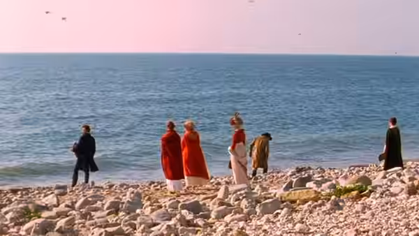 A group of people walks across a rocky beach beside the sea