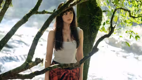 Cassandra Webb (Dakota Johnson) standing by a mossy tree with a spiderweb near rapids