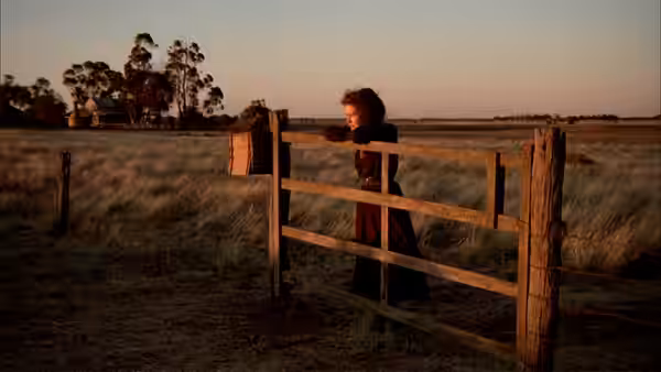 Harry Beecham (Sam Neill) leans on a wooden gate in an open field