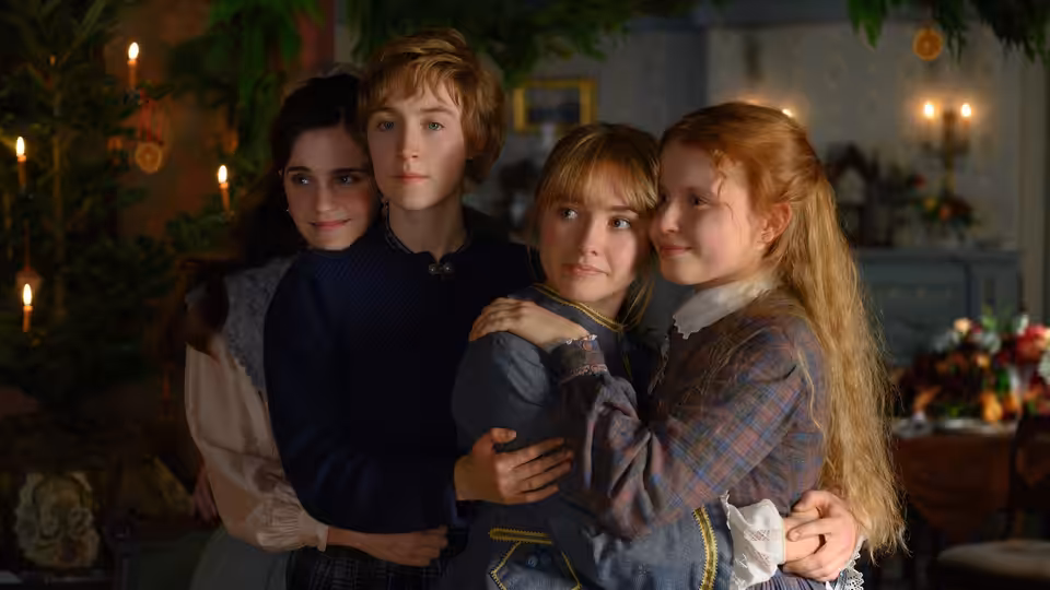 Four young women in period clothing embracing closely in a candlelit decorated room