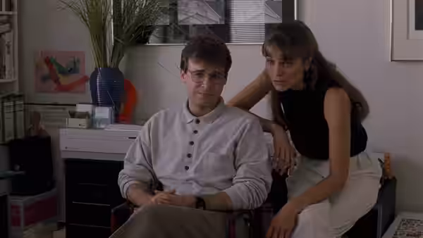 Nathan Huffner (Rick Moranis) sits beside Susan Buckman (Harley Jane Kozak) in a cluttered room