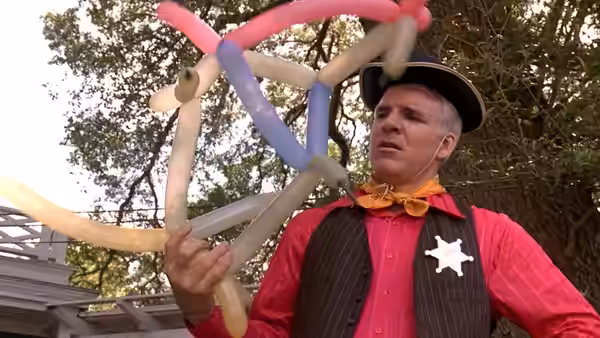 Gil Buckman (Steve Martin), dressed as a sheriff, holds a cluster of twisted balloons outdoors